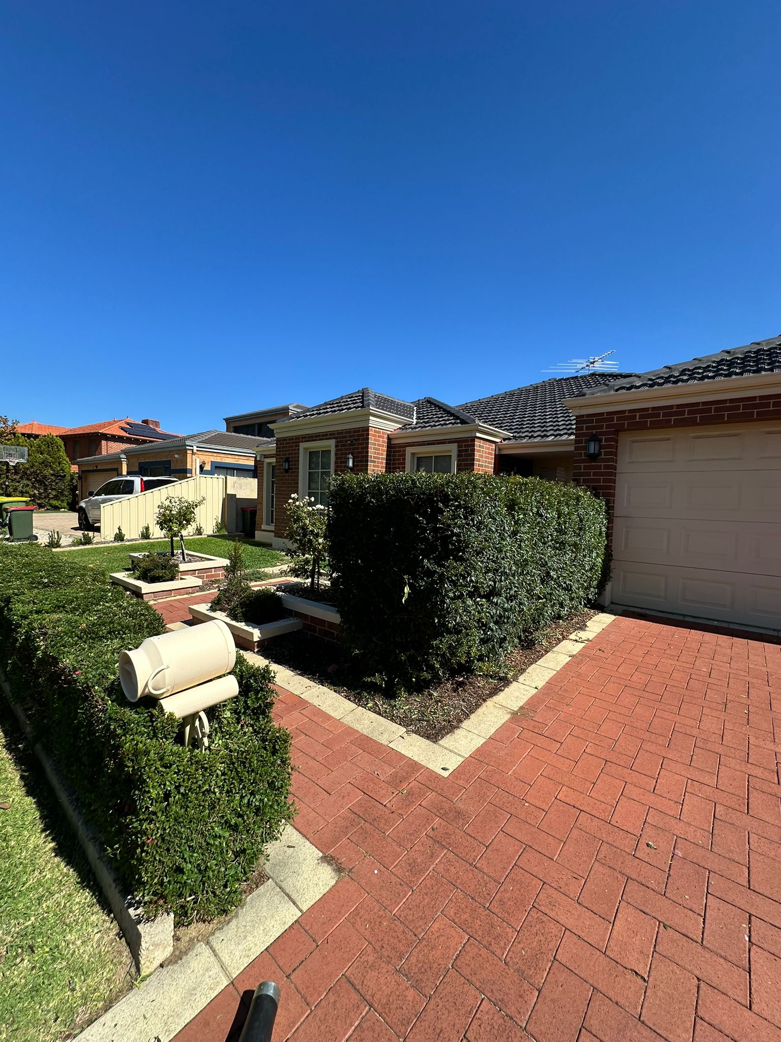 Trimmed hedge beside a mown front lawn and brick paving